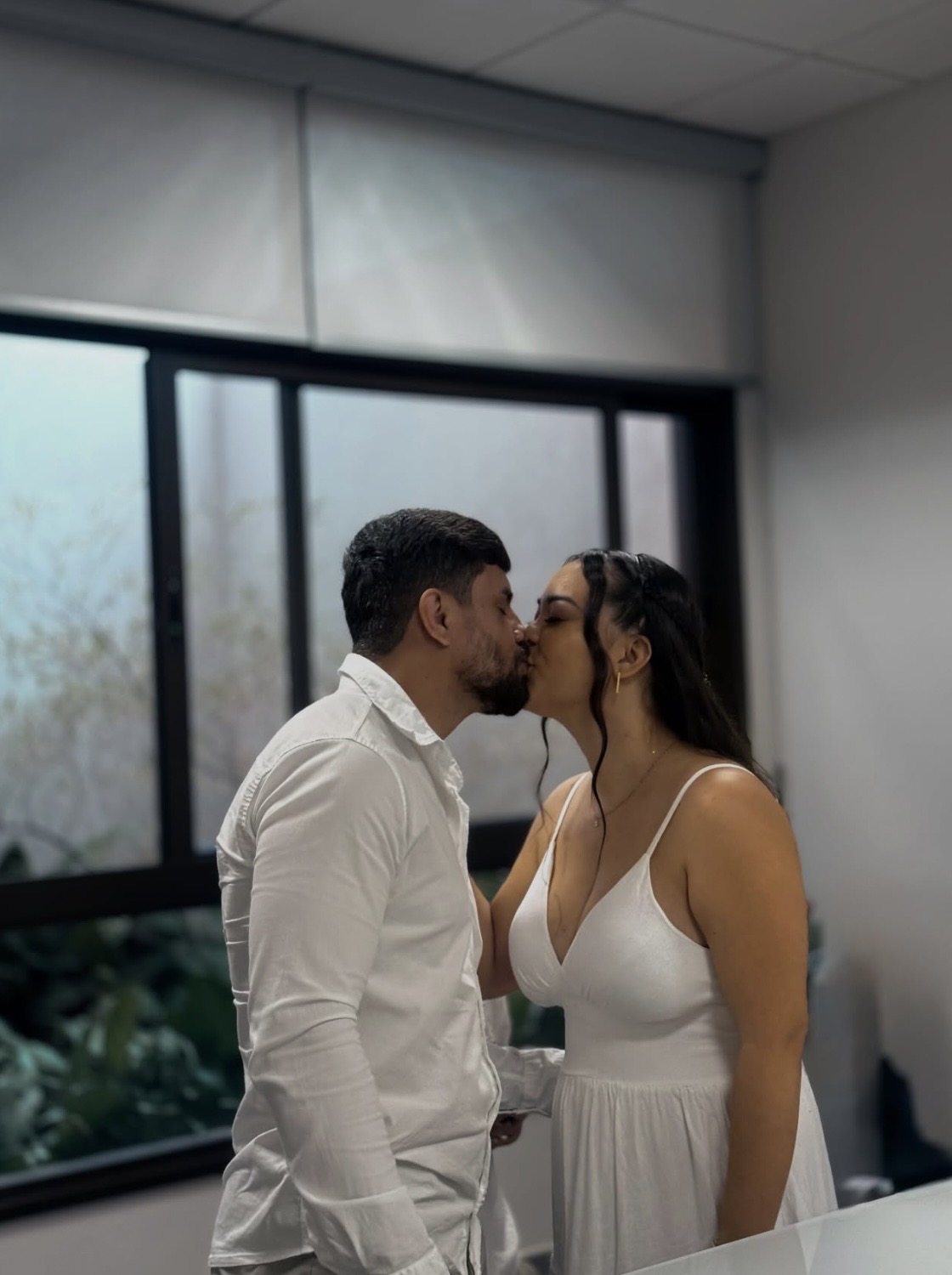 Casal se beijando em ambiente interno junto à janela